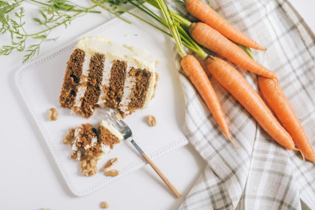 Slice of layered carrot cake with cream cheese frosting and fresh carrots