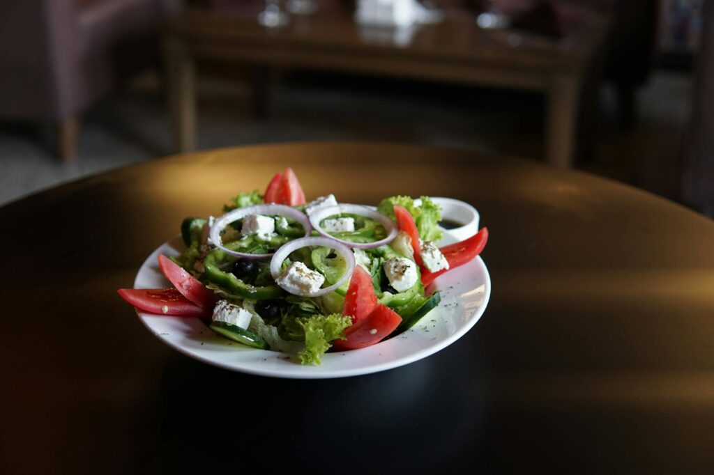 Greek salad with feta, tomatoes, olives, red onion and greens on a white plate