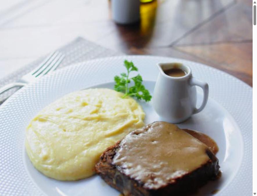 Classic homemade meatloaf with gravy served with creamy mashed potatoes on a white plate
