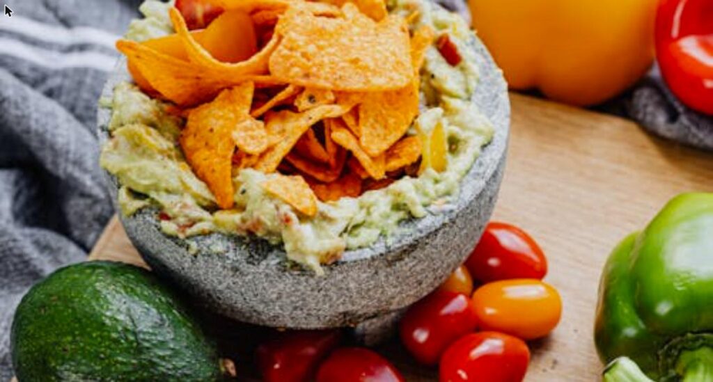 Fresh homemade guacamole in a stone bowl with tortilla chips, avocado, and tomatoes