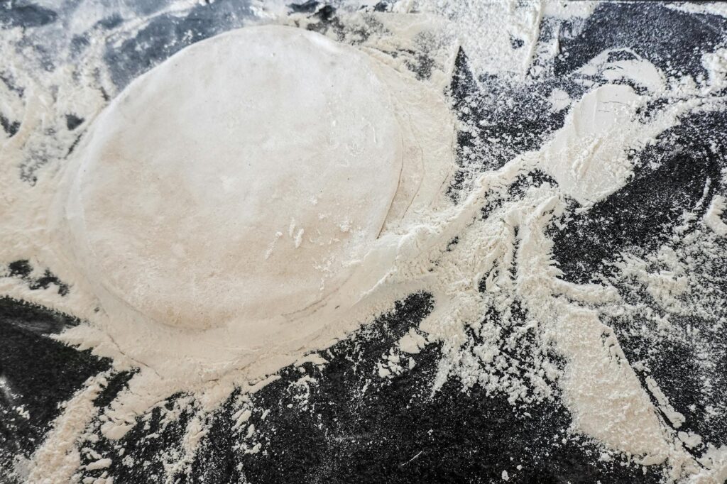 Easy homemade pizza dough on a flour-dusted dark surface, hand-stretched and ready to top