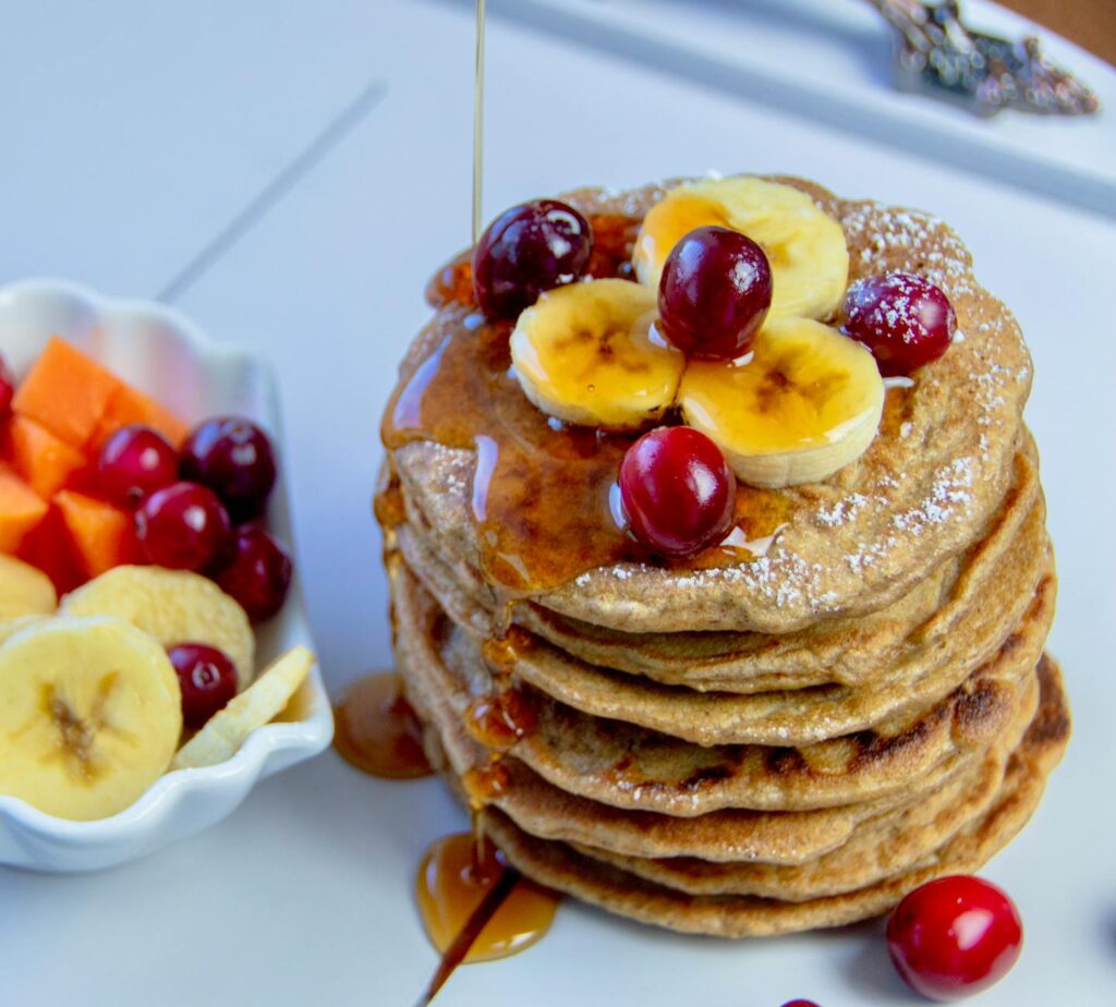 Easy banana pancakes stacked tall with sliced bananas, cherries, and syrup
